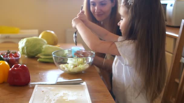 Óvodás, főzés a konyhában az anyja irányítása alatt a saláta. A lány a zöldségek só, hozzáteszi, fűszerek — Stock videók