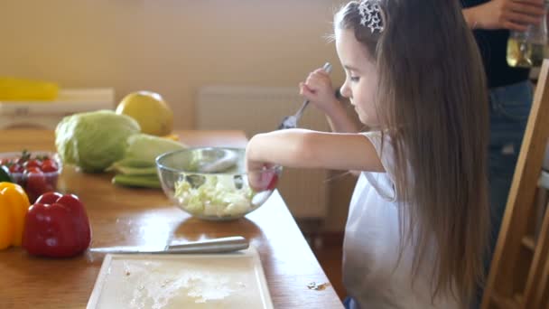 Proper nutrition. A child tries cherry tomato from lettuce in the kitchen. Moms helper — Stock Video