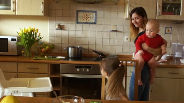 Schöne Mutter mit zwei Kindern, die in der Küche das Abendessen zubereitet. Hausfrau im Mutterschaftsurlaub. Vorschulkinder gesunde Ernährung — Stockvideo