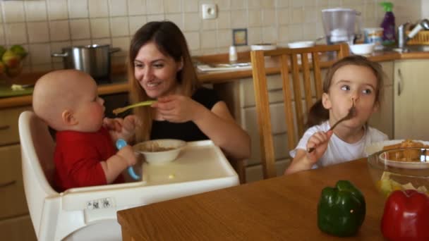 La madre alimenta al bebé sentado en la trona. El niño no quiere comer y agarra una cuchara con la mano. Día de las Madres — Vídeos de Stock