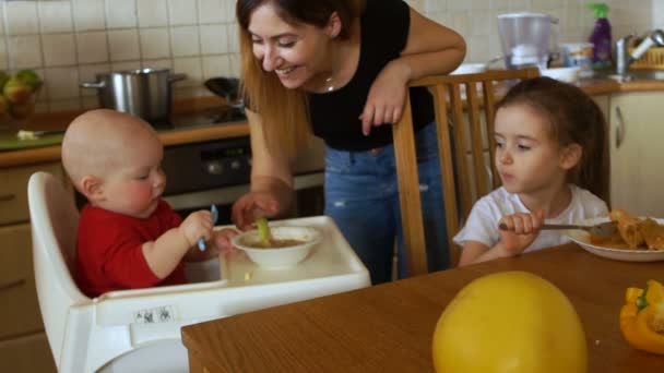 La ama de casa en la cocina alimenta a su hijo y a su hija para la cena. Día de las Madres — Vídeos de Stock