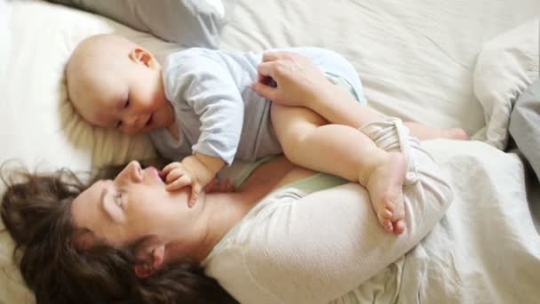 La madre matura gioca con il bambino sdraiato a letto. Il bambino tocca il dito alla bocca della madre, lo sviluppo dei bambini — Video Stock