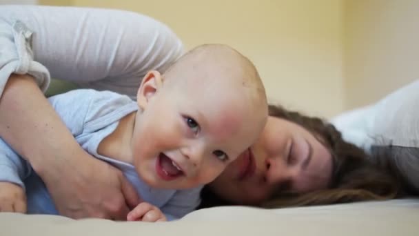 Bayi ceria pada usia satu tahun berbaring di tempat tidur dengan ibunya dan tertawa — Stok Video