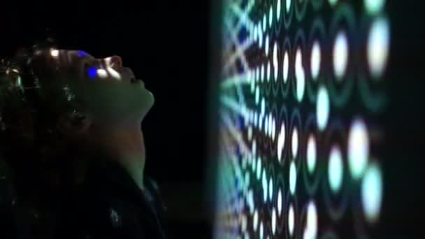 Ein Kind blickt auf den oberen Rand einer riesigen, leuchtenden Leinwand mit abstrakten Mustern. Zukunftstechnologien, das Spiel von Licht und Schatten — Stockvideo