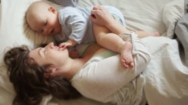 Mutlu genç anne bebek yatakta ile oynarken. Parmağını ağzına bir anne, çocuk gelişimi çocuk dokunur
