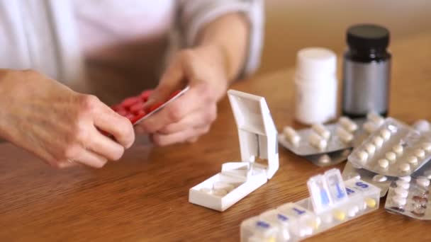 Eine ältere Frau zieht eine Tablette aus der Verpackung und teilt sich mit einem speziellen Plastikbehälter in Teile. Apothekenkonzept. Hände von Arthritis-Patienten — Stockvideo