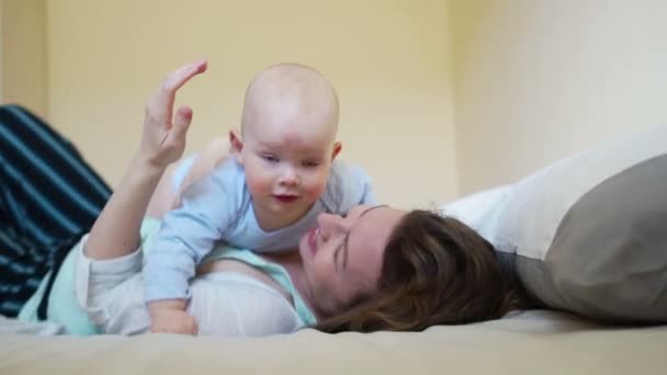 Mamá y el bebé se divierten en la cama el fin de semana. Feliz fin de semana familiar — Vídeos de Stock