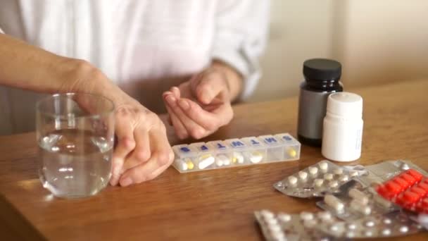 Пенсионер смывает таблетку с водой из стакана. Концепция аптеки. Руки старухи на фоне бутылок и волдырей с таблетками — стоковое видео