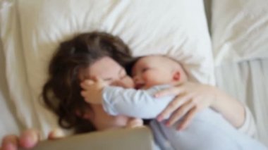 Anne ve bebek yatakta yatan selfie olun. Bebeğim ısırıkları anne yanağından, eğlenceli aile hafta sonu