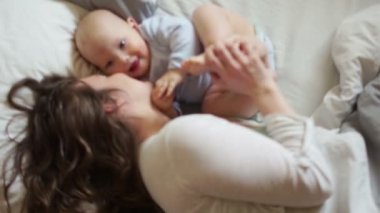 Sevgi dolu bir anne küçük oğlu onunla beyaz yatakta yatan gıdıklıyor. Yumuşak odak