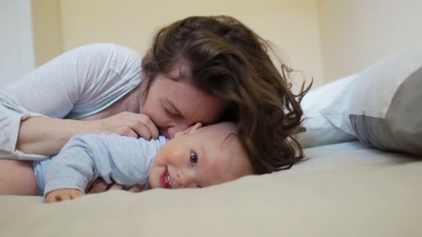 Schöne lockige Frau küsst und umarmt ein einjähriges Kind. Mutter und Kind kitzeln und lachen — Stockvideo