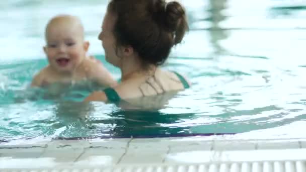 El bebé nada con su madre en la piscina cubierta. El niño está feliz y apasionado por el proceso, el día de las madres — Vídeo de stock