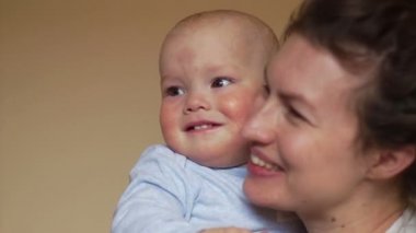 Oğlu tutan anne. Ellerini sallayarak ve gülümseyerek. Bebeklerin gelişimi kadar bir yıl, anneler günü