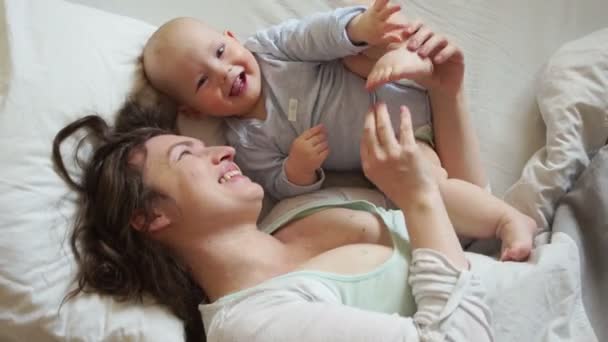 母の愛。赤ちゃんと朝を抱いて笑顔でベッドの母親。幸せな家族で、母の日。出産の概念 — ストック動画