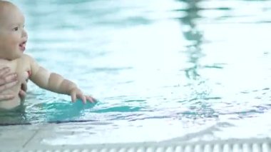 Genç annesinin ellerindeki çocuk evin kenarındaki havuzda yüzüyor. Çocuk mutlu ve tutkulu. Anneler günü, mutlu aile hafta sonu, çocuklar spor