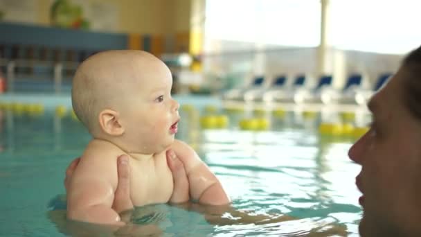 Papá enseña a los niños a bucear en la piscina cubierta. Entrenamiento individual en la piscina para niños de hasta un año. Desarrollo infantil — Vídeo de stock