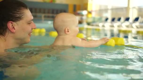 A criança e o pai divertem-se na piscina grande. A criança brinca com os carros alegóricos amarelos, o pai apoia-o — Vídeo de Stock