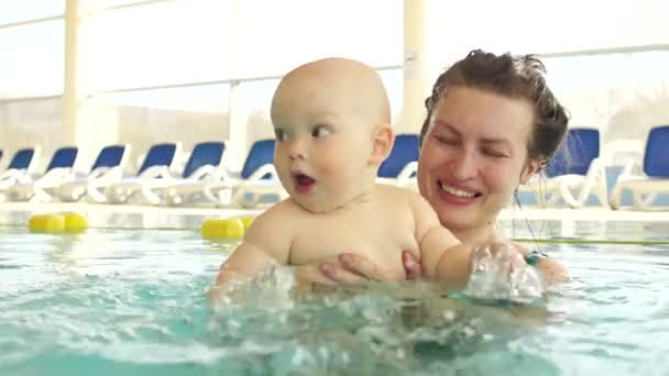 Roztomilé dítě v náručí z její matky se učí plavat v bazénu. Dítěti zábavné šplouchání ruce do vody, tryskající fly. Detail — Stock video