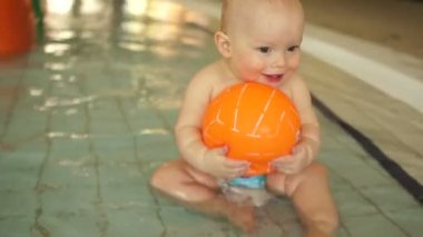 Bir su parkı çocuk sıcak havuzda otururken bir turuncu topu ile oynayan harika çocuk