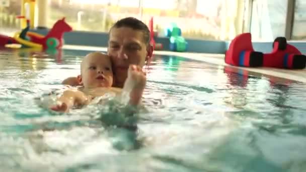 Trainer bringt dem Baby das Schwimmen im Pool bei. Das Baby liegt auf dem Rücken und lernt, mit den Füßen zu rudern. Individuelles Training, Vatertag — Stockvideo