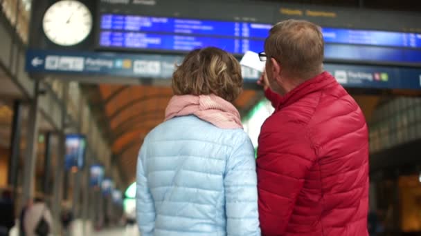 Coppia matura alla stazione controlla i biglietti con gli orari. Un uomo bacia una donna sulla fronte e vanno al treno — Video Stock