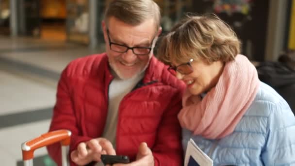 Man och hustru skrattar, tittar på foton i smartphonen. Nära porträtt av en glad äldre par — Stockvideo