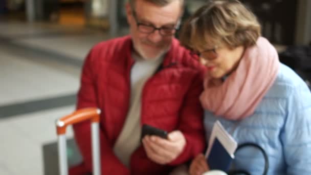 Mujer y hombre mirando la pantalla del teléfono inteligente y sonriendo felizmente. El par están vestidos con chaquetas de primavera, ambos llevan gafas, una hermosa bufanda rosa está en la mujer — Vídeos de Stock