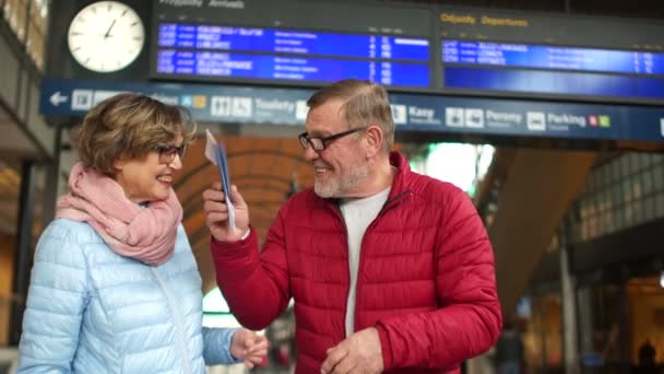 Boldog nyugdíjas pár a vasútállomásnál. Egy ember viccesen integetett útleveleket és jegyeket, egy nő veszi őket a kezében — Stock videók