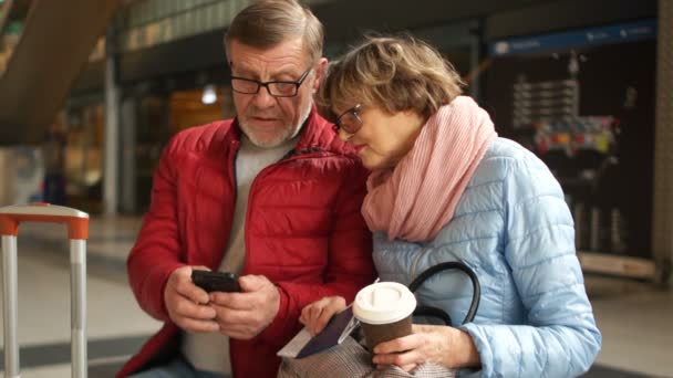 Gelukkige man en vrouw Foto's bekijken van de reis zittend op een bankje in het station te wachten op een trein — Stockvideo