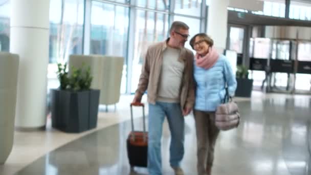 Atractivos jubilados marido y mujer van a la terminal del aeropuerto para embarcar. La pareja está hablando animadamente y sonriendo el uno al otro — Vídeo de stock