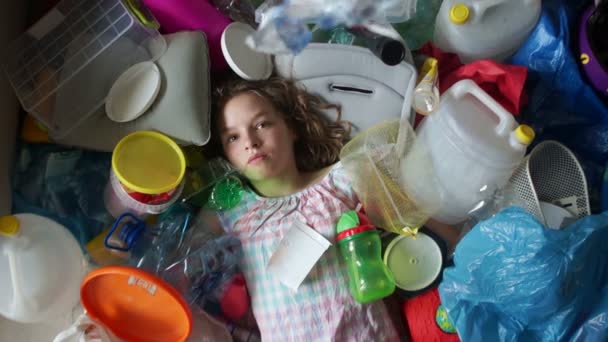 Ecologische concept, de dreiging van plastic vervuiling. Het meisje ligt in een stapel van multi-gekleurde kunststof. Vuilnis valt op haar, ze huwt — Stockvideo