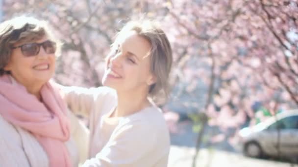 Beautiful sunny spring portrait of mother and daughter. Two women hugging and laughing against the backdrop of sun glare and flowering trees — Stock Video