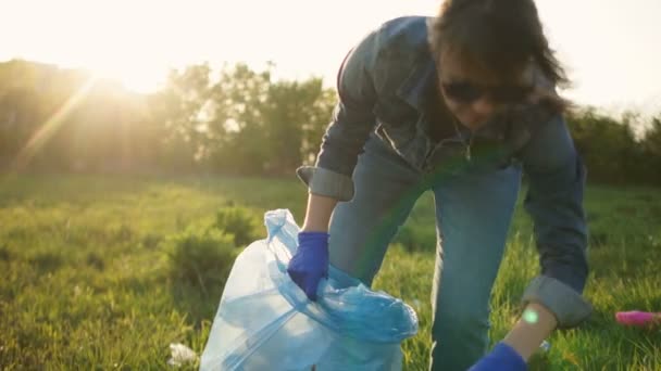 Mujer voluntaria recogiendo basura en un parque de la ciudad. El sol poniente, los reflejos brillantes, el tiempo ventoso. Concepto social — Vídeo de stock