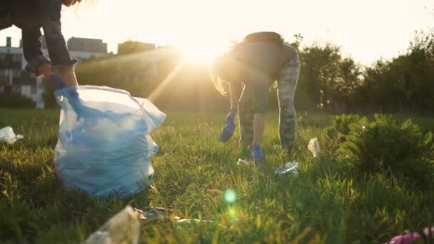 I volontari sociali portano fuori la spazzatura nel parco primaverile e la mettono in un grande sacchetto di plastica. Ferma plastica — Video Stock