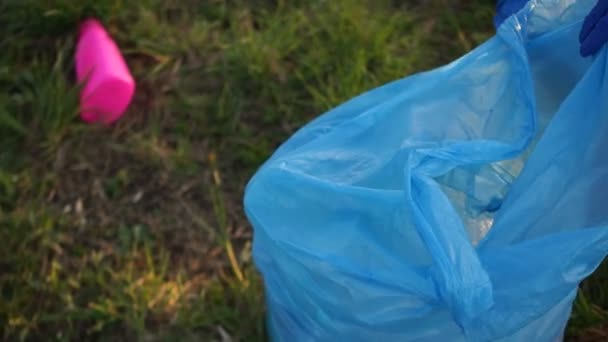 Clasificar basura, concepto ambiental, detener el plástico. Primer plano de una mano voluntaria recogiendo basura en una gran bolsa de plástico azul — Vídeos de Stock