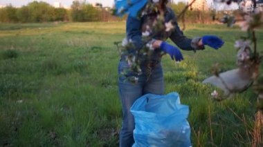 Evsel atık sorunu, plastik durdurmak, sıfır atık. Gönüllü bir kız güzel bir çiçek açan elma ağacının dalları altında parkta çöp toplar
