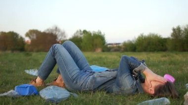 Parktaki çimenlerin üzerinde plastik çöpün ortasında yatan kot takım elbiseli bir kızın portresi. Kamera etrafta dolaşıyor ve yükseliyor. Dur plastik, evsel atık sorunu, sıfır atık hareketi