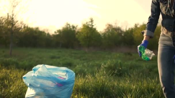 Mujer activa limpia el parque de escombros, plegándolo en una bolsa de plástico azul, toma el paquete en sus manos y sale del marco. El trabajo del voluntario ambiental — Vídeo de stock