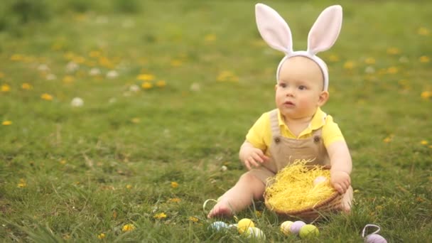 Il bambino vede prima le uova di Pasqua. Si tiene in mano e grida di felicità seduto sull'erba del parco. Buona famiglia pasquale — Video Stock