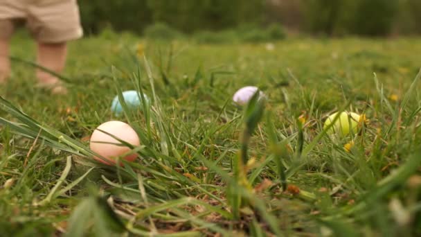 Close-up de ovos de Páscoa na grama contra o fundo dos pés de uma criança coletando ovos. Caça ao ovo de Páscoa — Vídeo de Stock