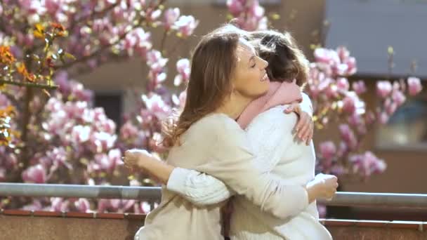 Fille étreint une mère âgée dans le contexte d'un magnolia florissant. Mère et fille se félicitent à l'occasion de la fête des mères — Video