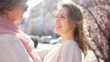 Genç, güzel kız, Rogod caddesinin ortasında çiçek açan bahar ağaçlarının arkasında duran olgun annesine sarılıyor. Anneler ve Kızları, Anneler Günü