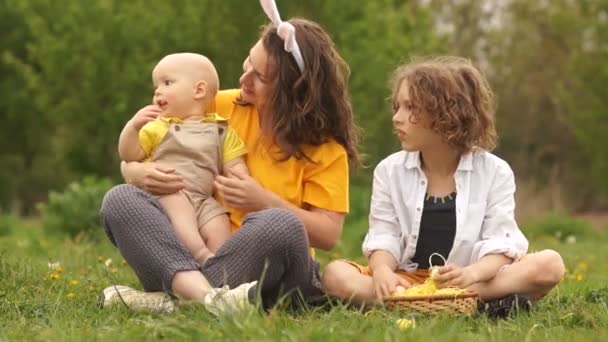 Curly doce mãe e seus dois filhos no parque em um piquenique. Feliz família da Páscoa. Dia das Mães — Vídeo de Stock