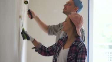 Yeni evlerinin duvarlarını boyarken boya silindirli genç kadın ve adam. Mutlu yeni evliler yeni evlerinde tamirat yaparlar.