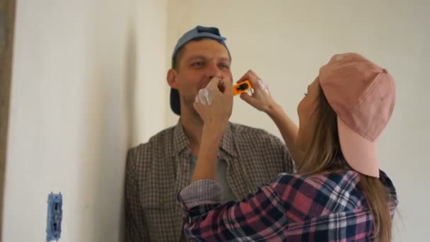 Pareja joven haciendo reparaciones en su nuevo apartamento. Recién casados felices, abrazando, riendo y bromeando — Vídeos de Stock