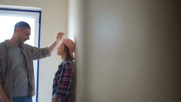 Ett kärleksfullt par omfamnar och skrattar i sin nya oreparerade lägenhet. Housewarming, nygifta och reparations koncept — Stockvideo