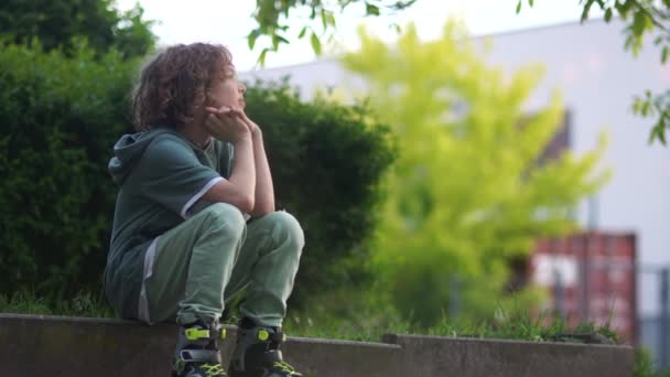 Szomorú gondolkodó iskolás a görgők ül a járdára, felszáll és levelek. Tini Roller, göndör fiú — Stock videók
