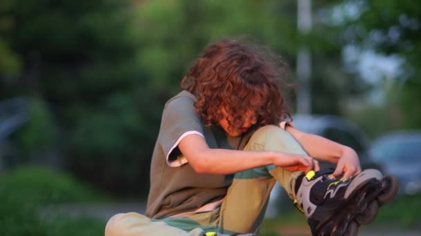 Krullend tiener zet op rollen in het Park. Schoolboy rollerblading, zonsondergang — Stockvideo