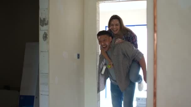 Housewarming, real estate, home renovation. Funny video young wife on the shoulders of her husband jumping on a new apartment during the repair — Stock Footage Housewarming, real estate, home renovation. Funny video young wife on the shoulders of her husband jumping on a new apartment during the repair Royalty Free Stock Video