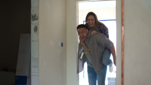 Housewarming, real estate, home renovation. Funny video young wife on the shoulders of her husband jumping on a new apartment during the repair — Stock Video